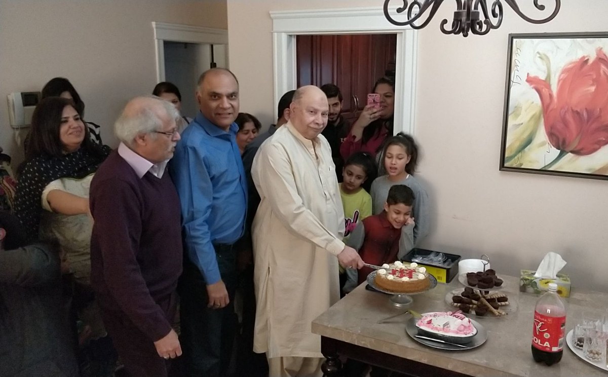 Aslam Hayat cutting the birthday cake, front-centre, surrounded by family