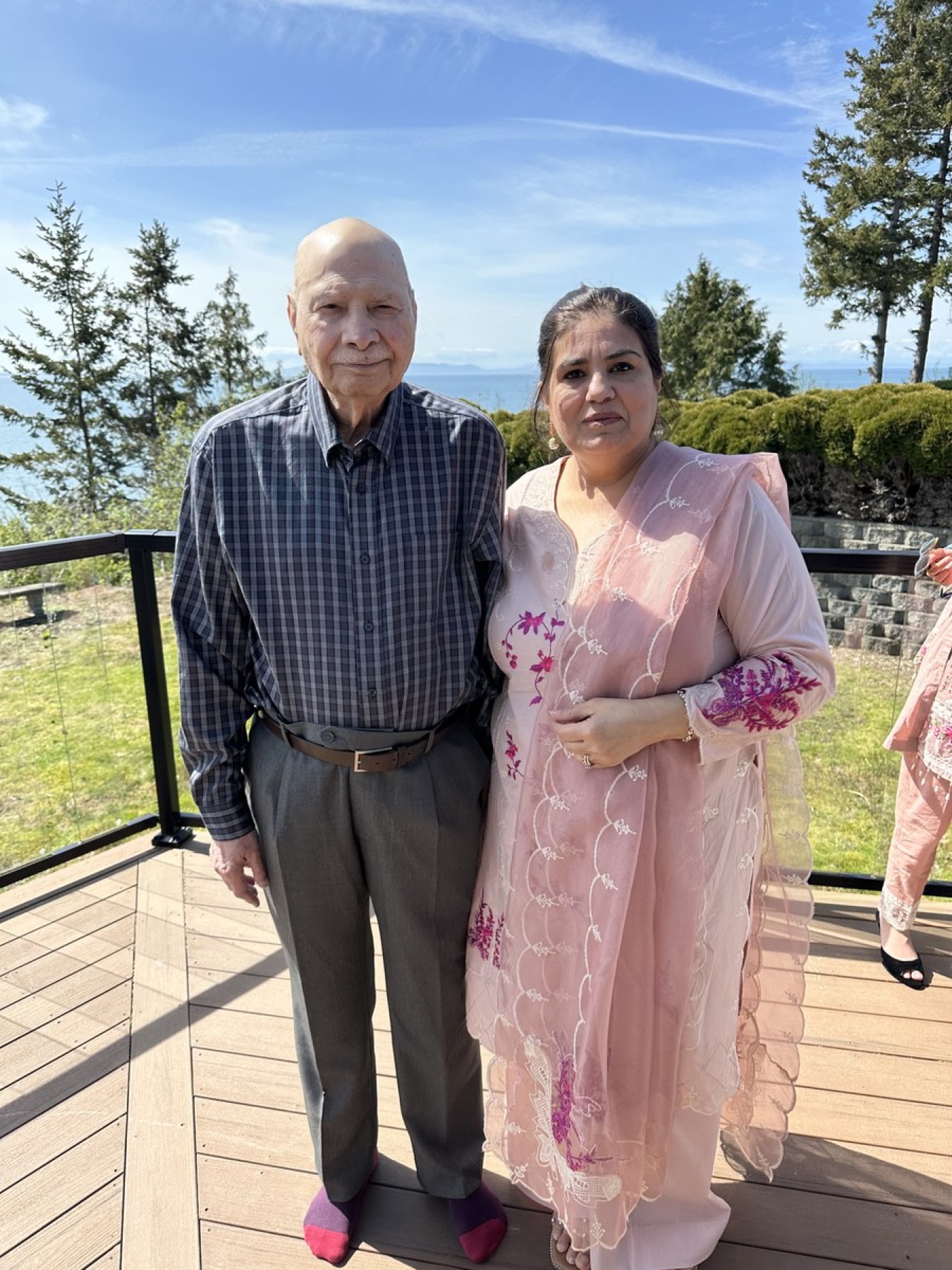 Aslam Hayat standing outdoors on a deck with a family member, British Columbia coast in the background
