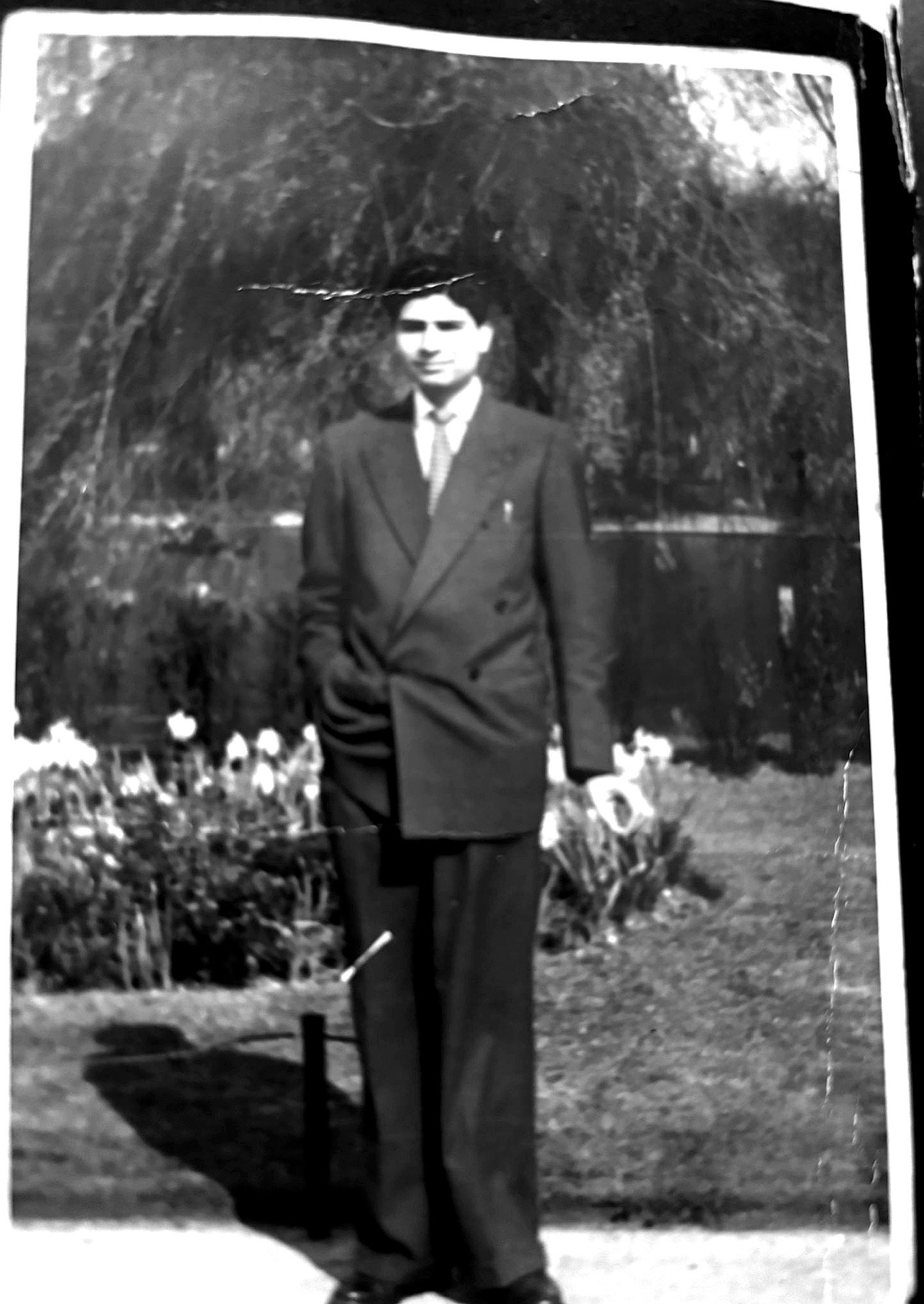Aslam Hayat as a young man standing in a garden, wearing a suit and tie